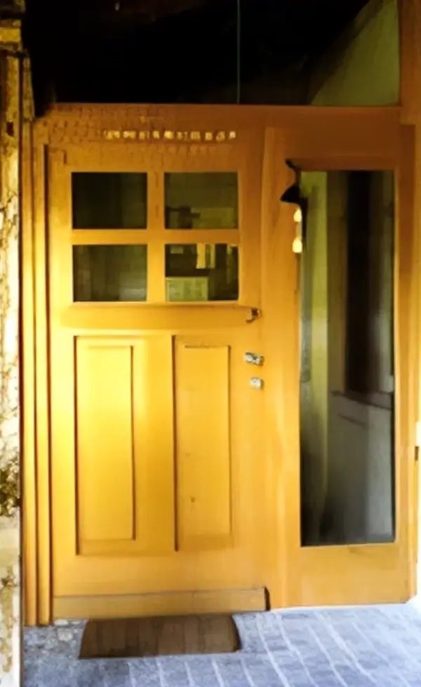 Eine sanierte und naturfarbene antike Eingangstür aus Holz.