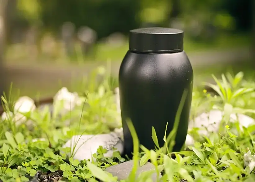 Schwarze schlichte Urne steht auf einem Grab